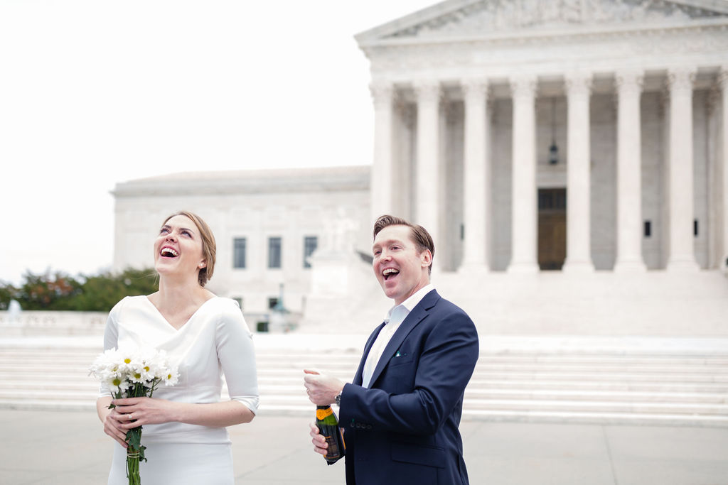 a groom with his bride popping a bottle of champagne on the day of their wedding 