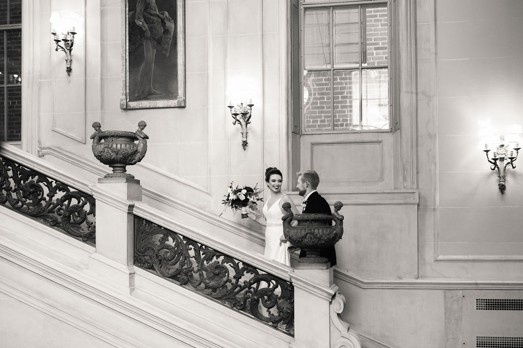 a couple walking up a set of stairs on the day of their wedding they are smiling at each other and the woman is holding a bouquet of flowers