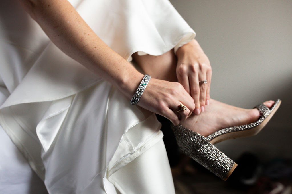a woman in a white wedding dress putting on a sparkly heel 