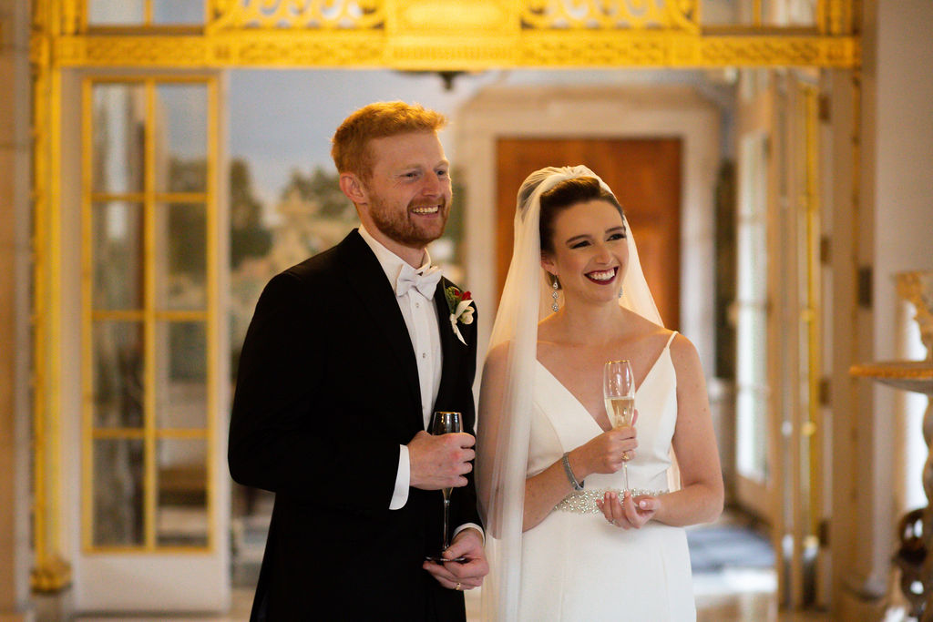 a couple holding champagne glasses and smilling at their wedding reception 