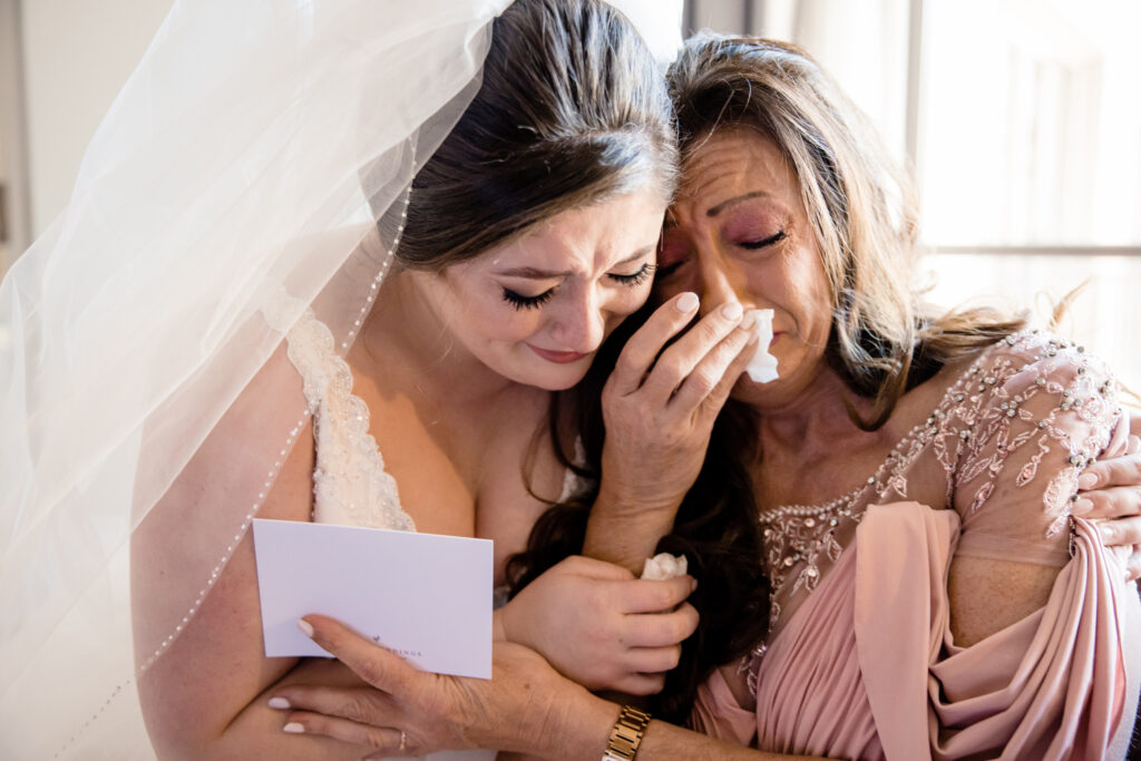 A person in a wedding dress hugging a family member as they both cry 