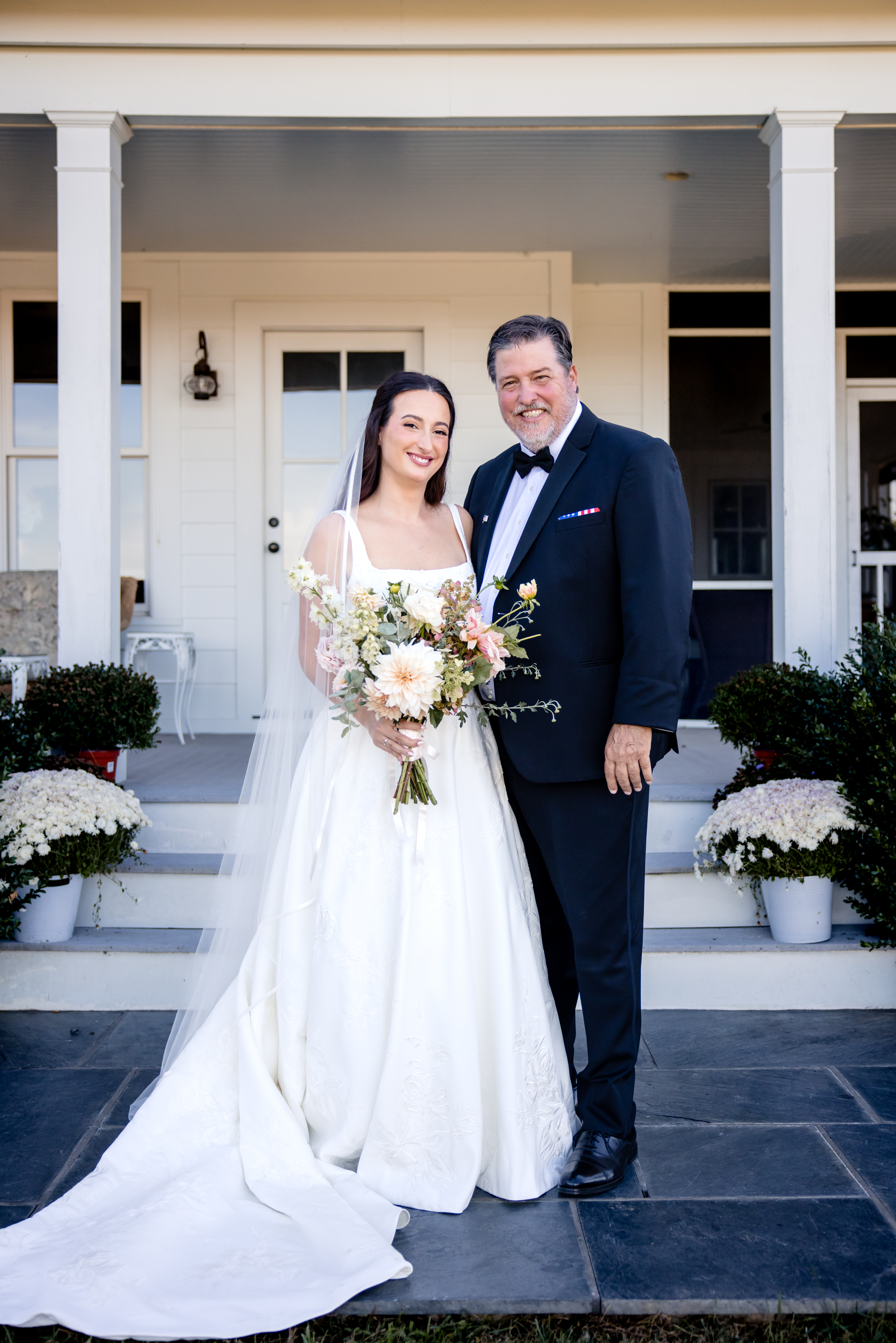 a bride on a porch taking a photo with her father 