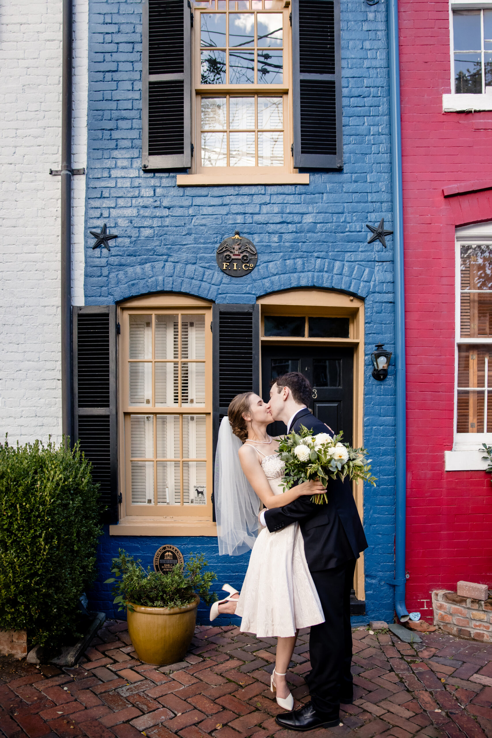 a couple kissing each other in front of a blue brick building on the day of their wedding 
