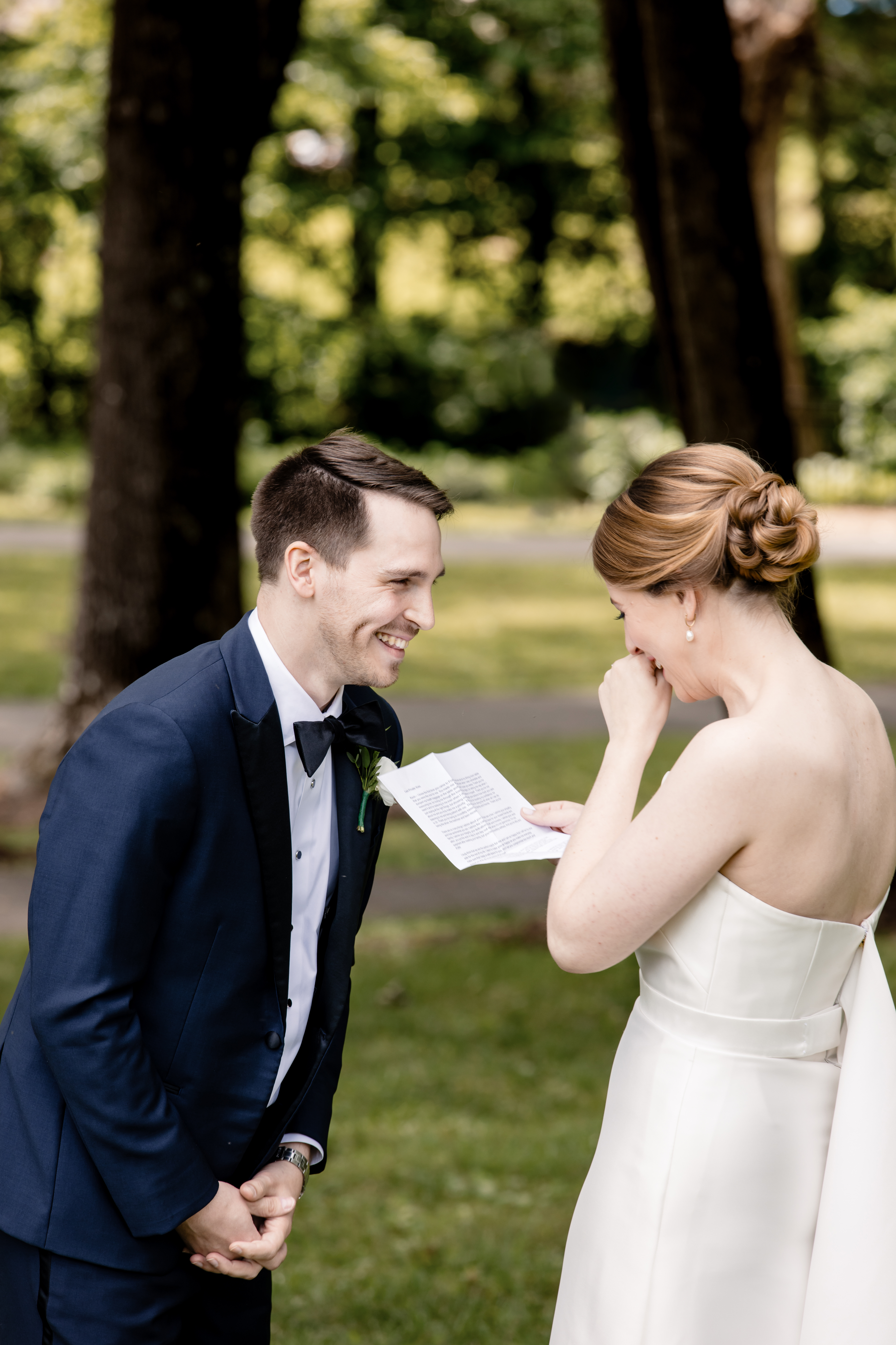 a bride laughing with her groom as she reads her vows to him 