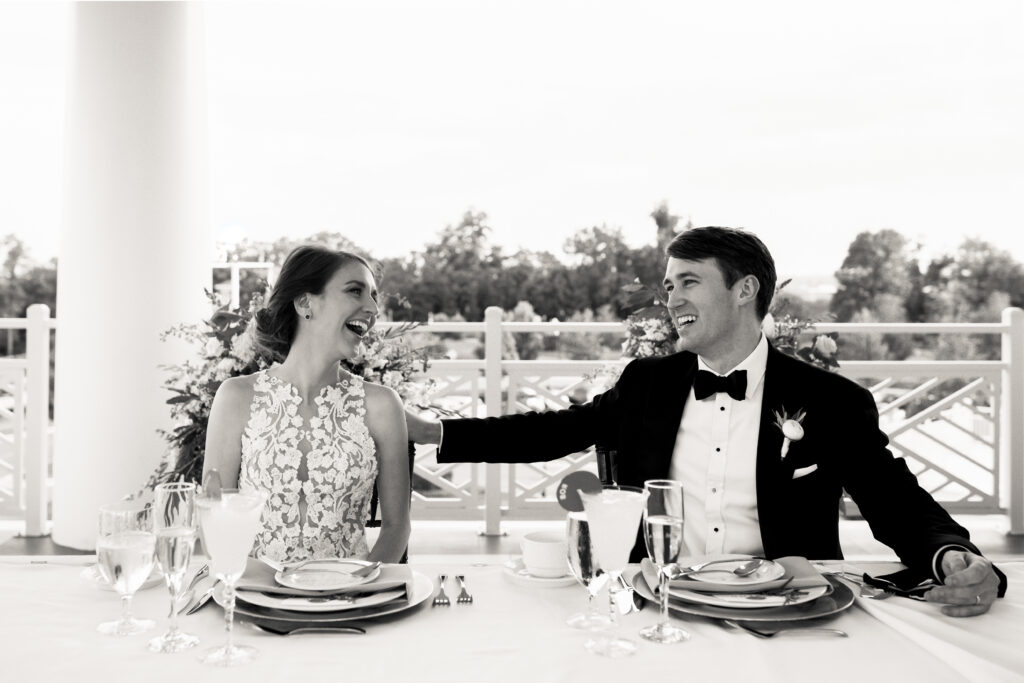 A newlywed couple laughing as they sit behind a table 