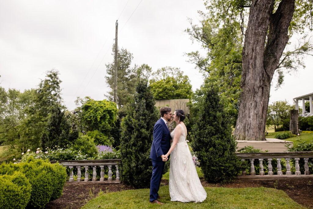 a couple holding hands in a garden leaning in for a kiss with each other