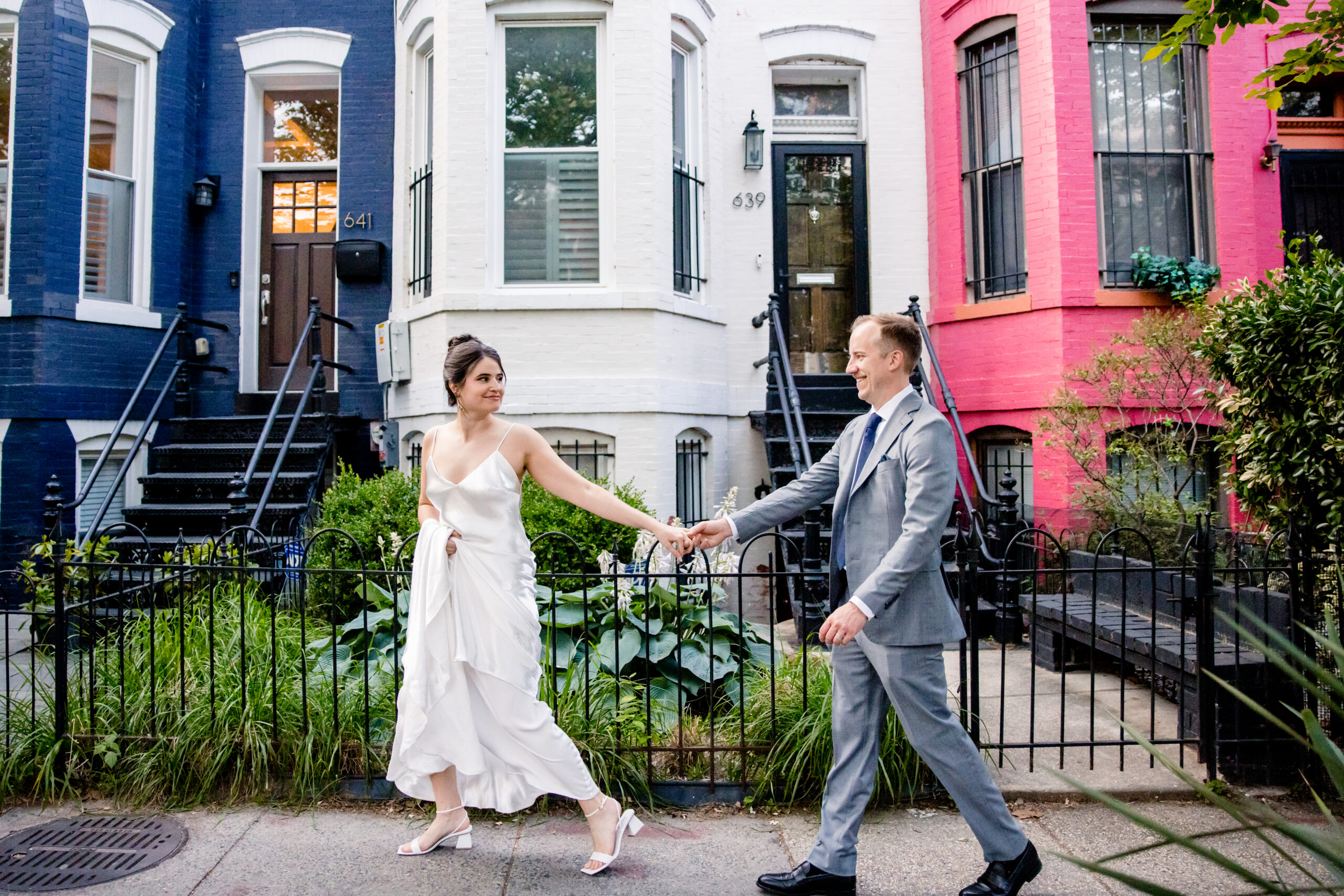 a couple walking hand in hand down a street together on the day of their wedding in front of a row of colorful houses