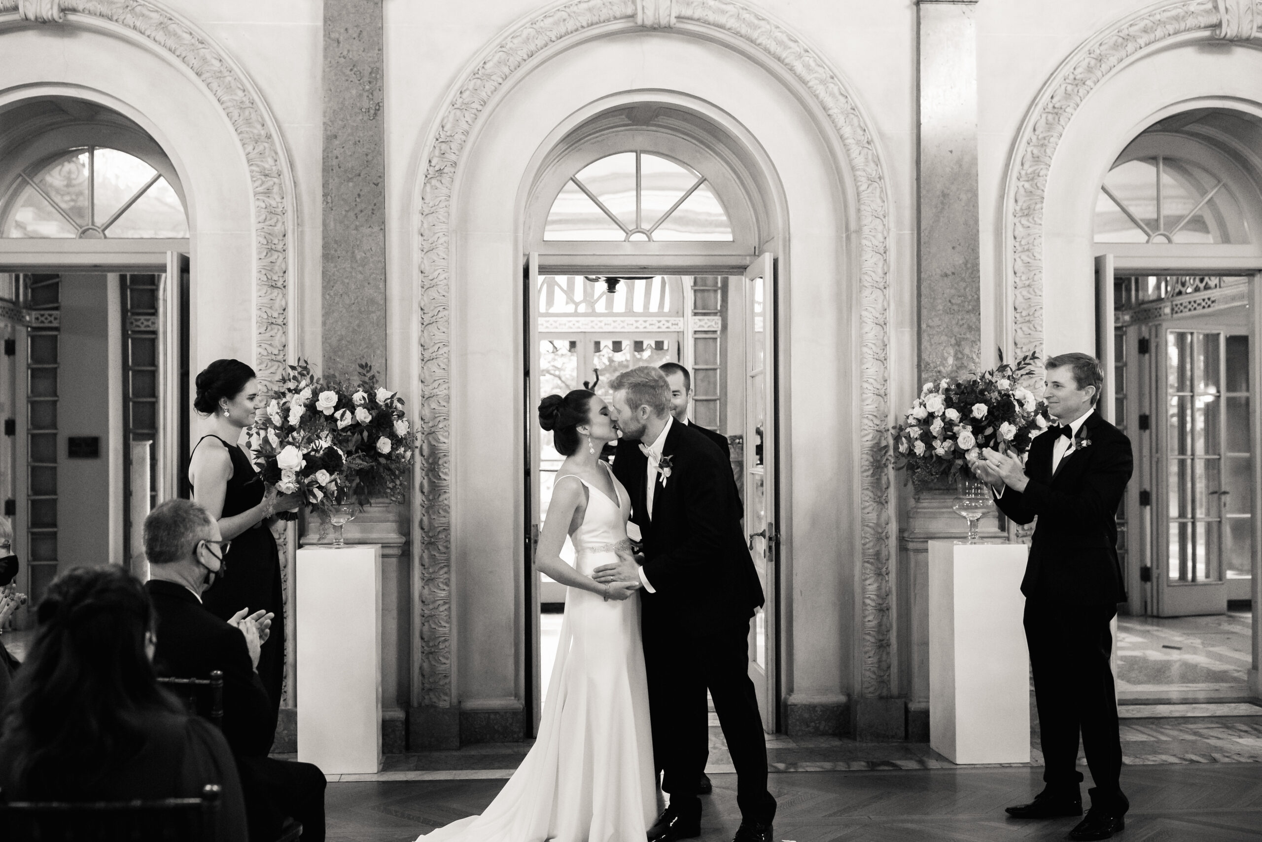 a bride and groom kissing at their wedding ceremony while their guests cheer for them