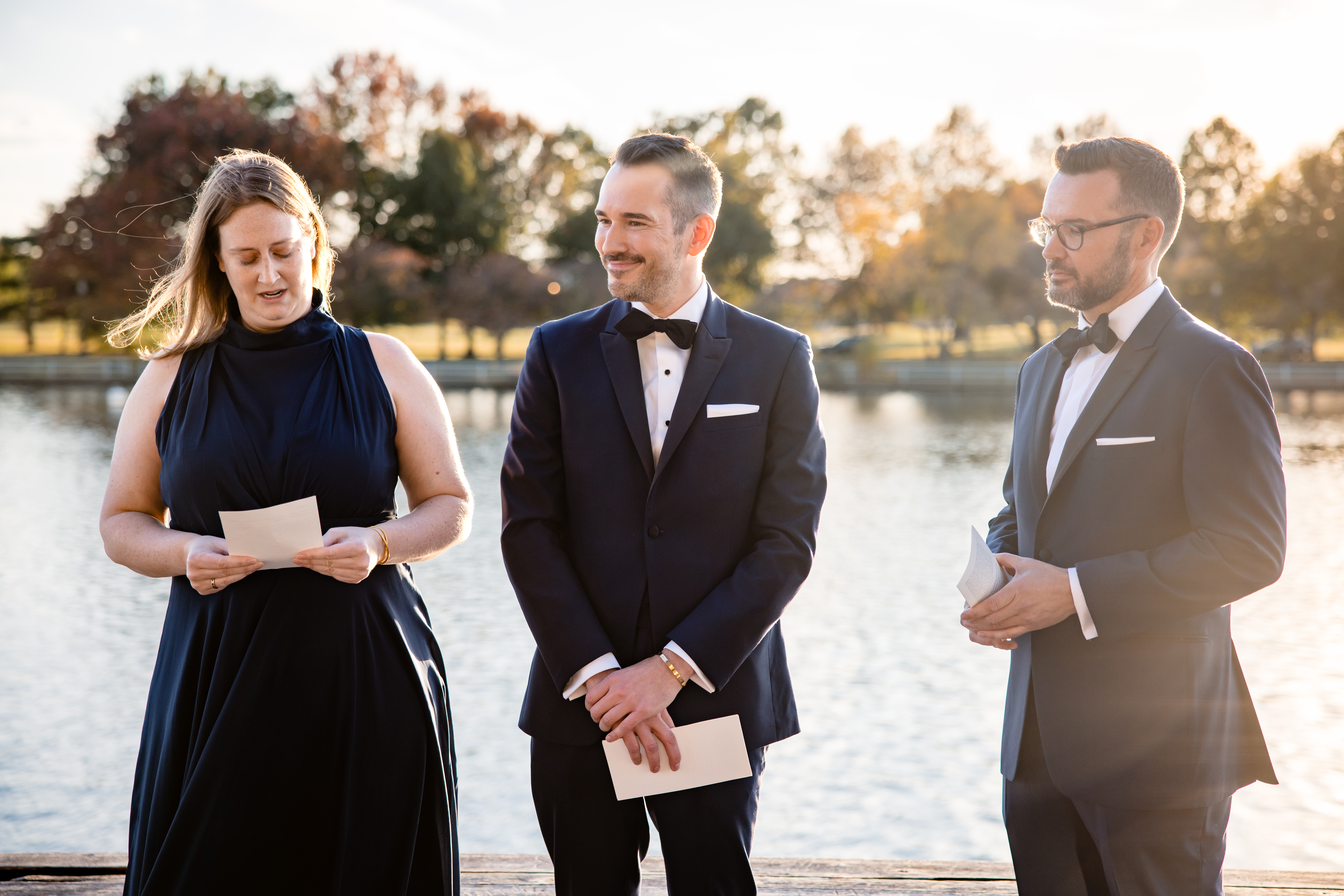 a small wedding party standing next to the water and holding speeches they've written for the wedding