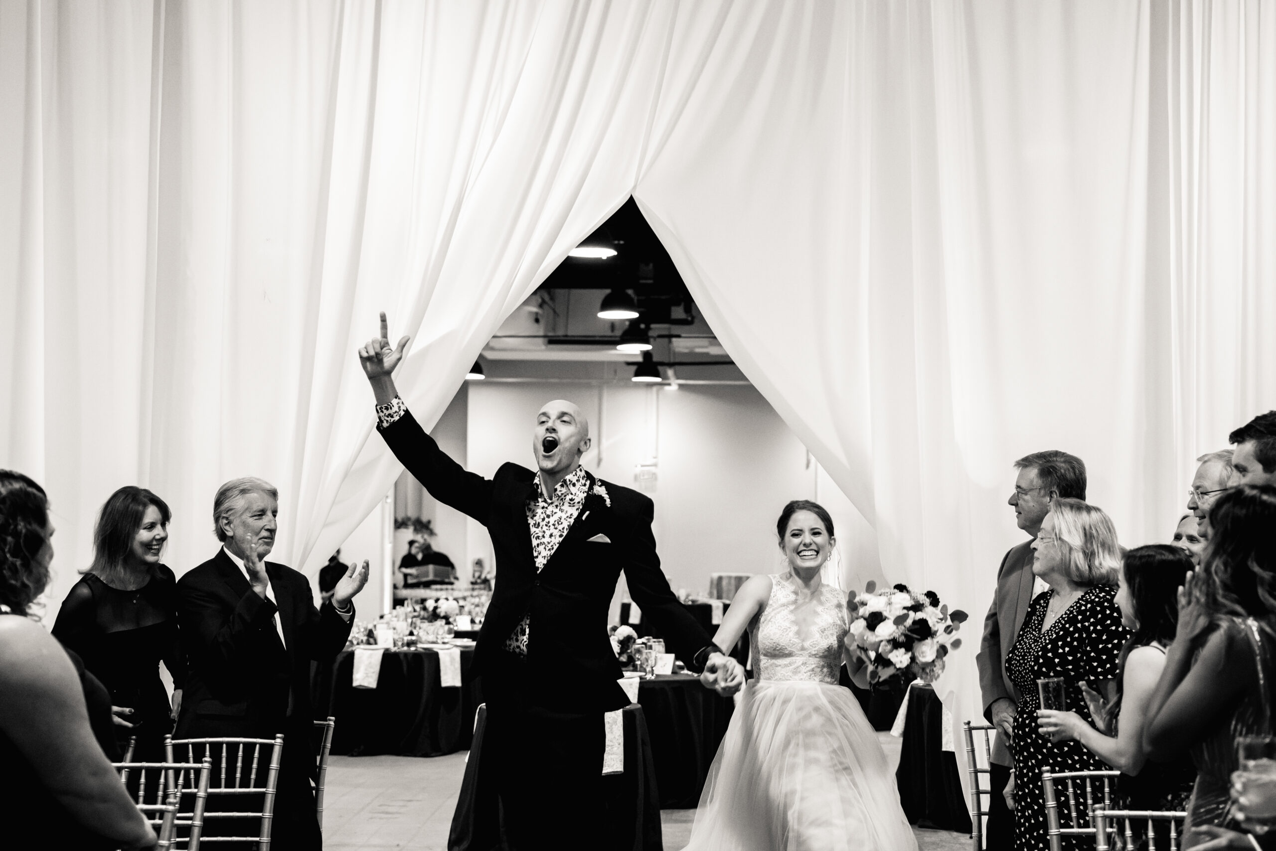 a bride and groom entering their wedding reception as their guests stand and clap for them