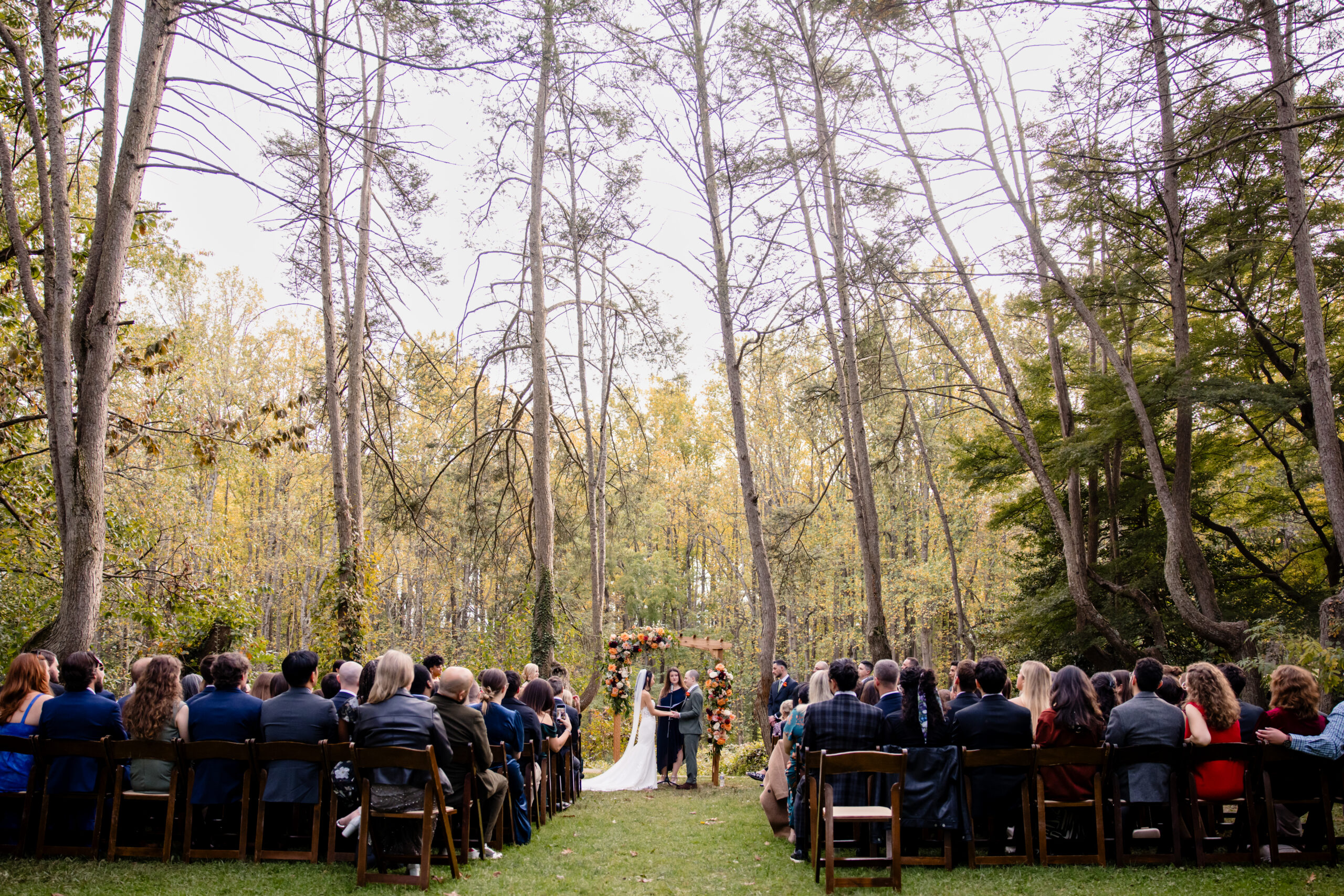 a bride and groom having an outdoor wedding ceremony underneath of trees