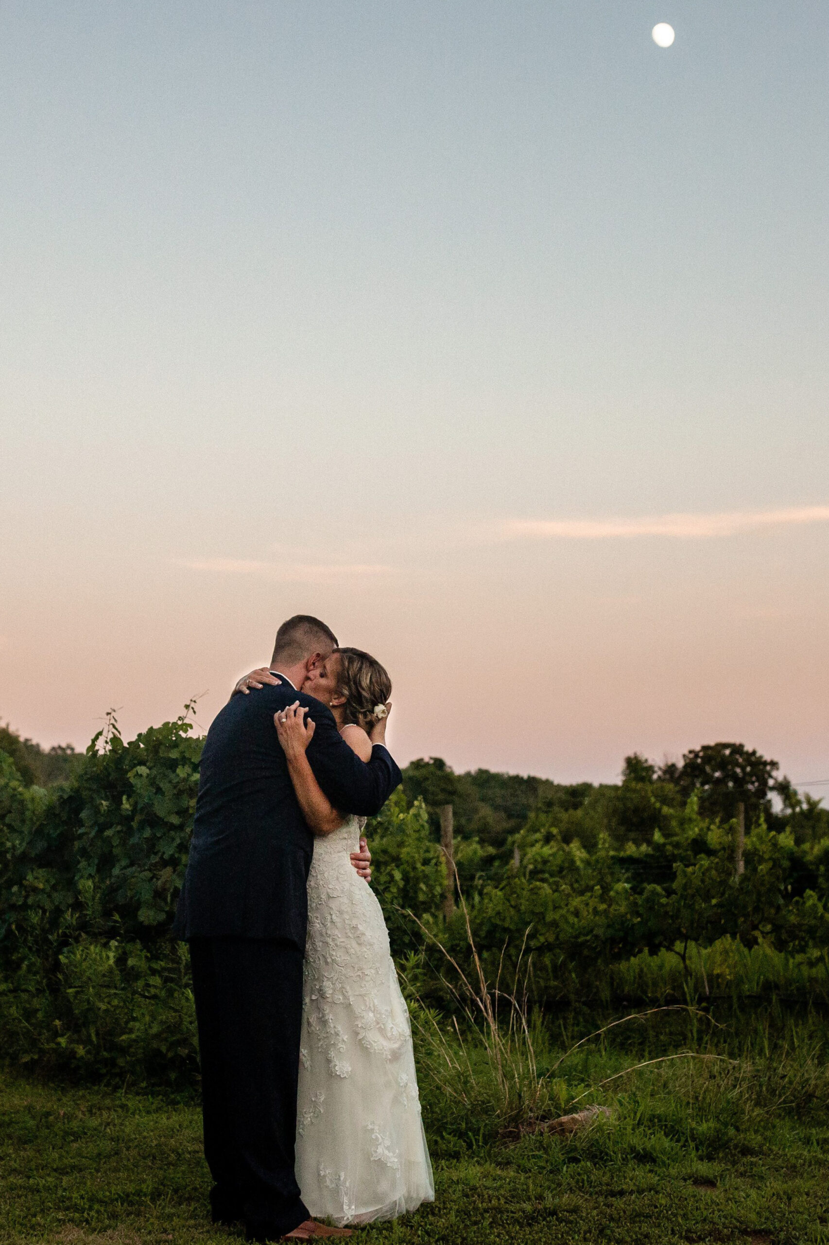 a bride and groom embracing in a field at sunset 