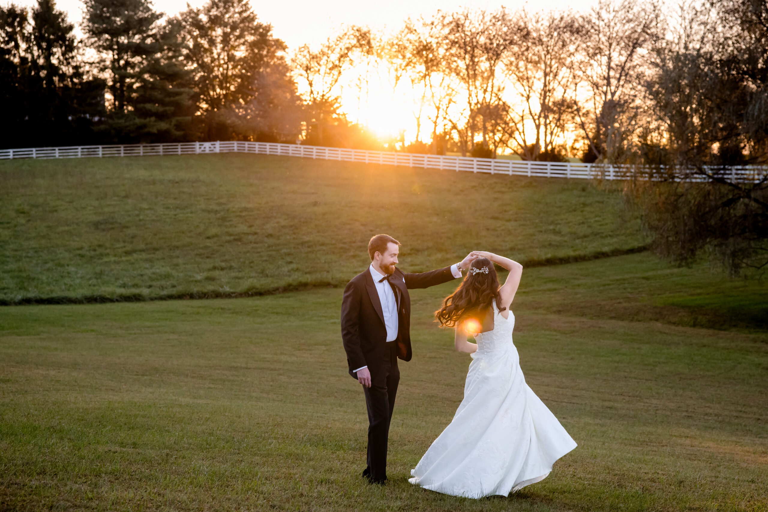 a bride and groom dancing on a lawn at sunset together the groom is twirling the bride around 