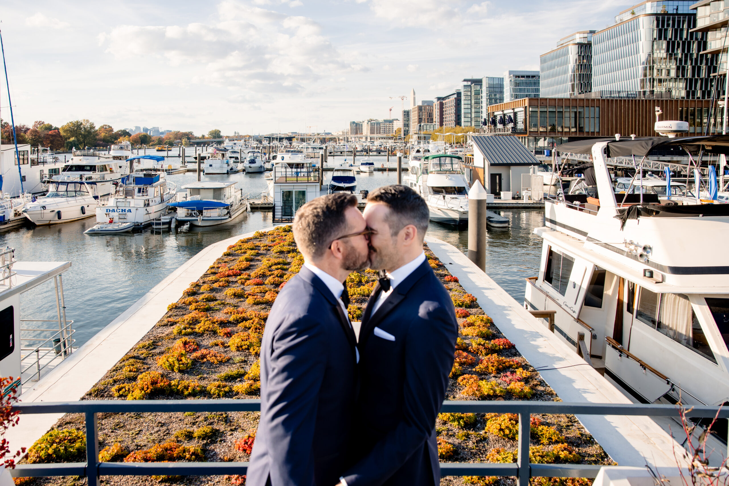 two men kissing on a boat dock on the day of their wedding 