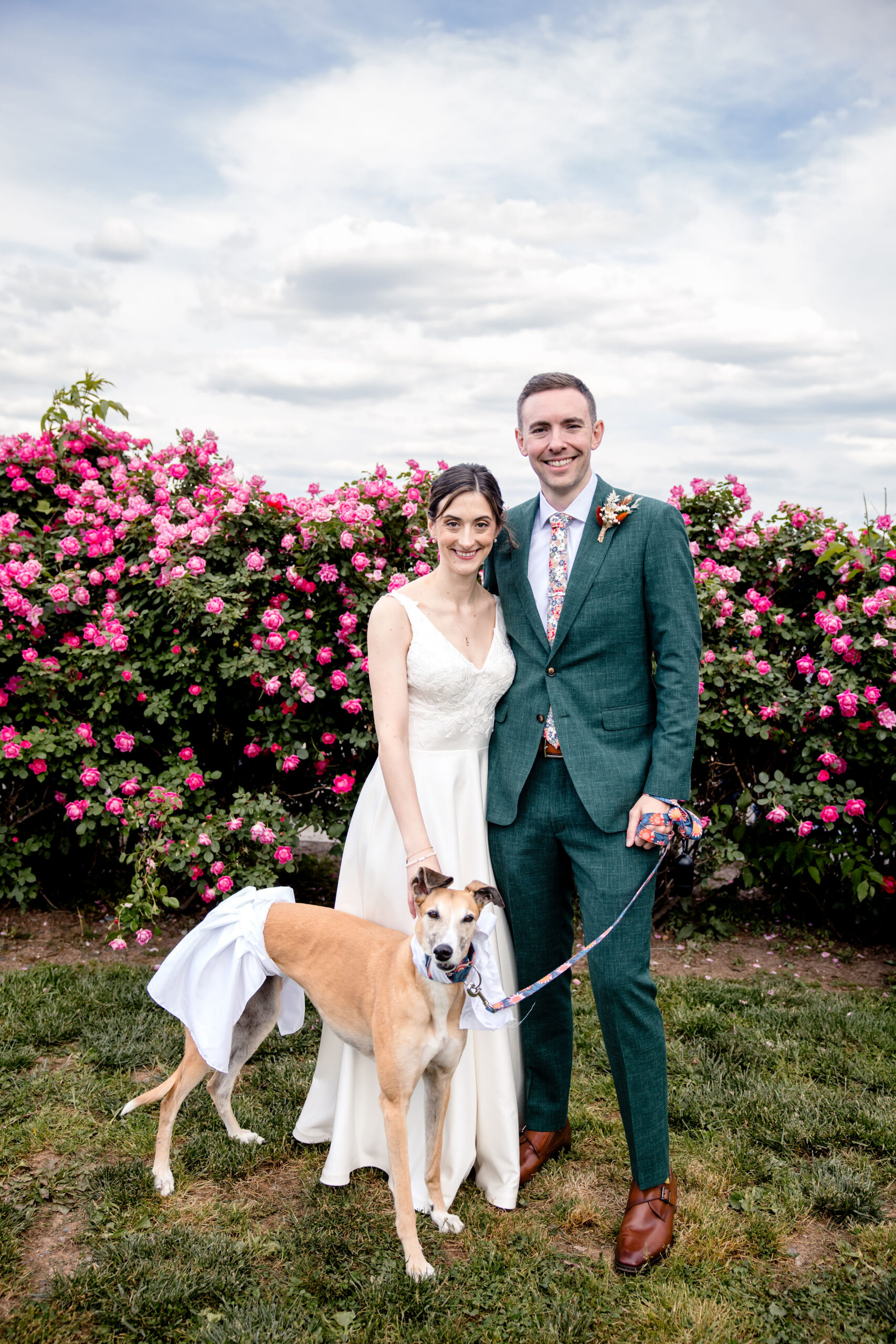 a man and woman posing in front of flowers on the day of their wedding with their dog 