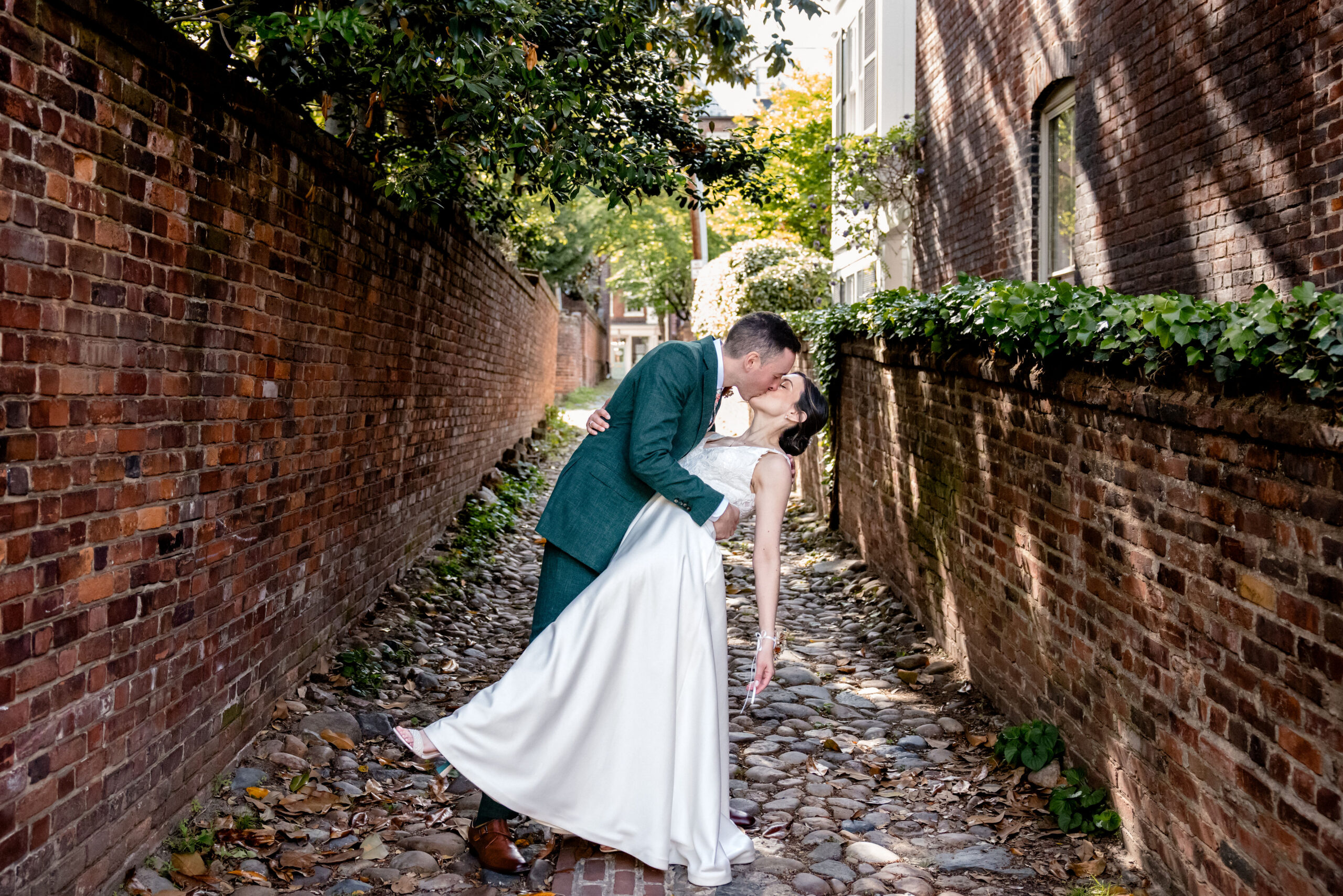 a man dipping a woman backwards in a brick alley in old town alexandria and kissing her on the day of their wedding