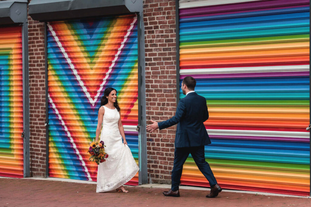 A couple walking towards each other to hug in front of a colorfully painted wall 
