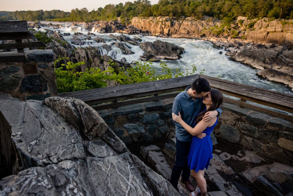 A couple with their arms around each other as they lean in to kiss in front of a rushing river 