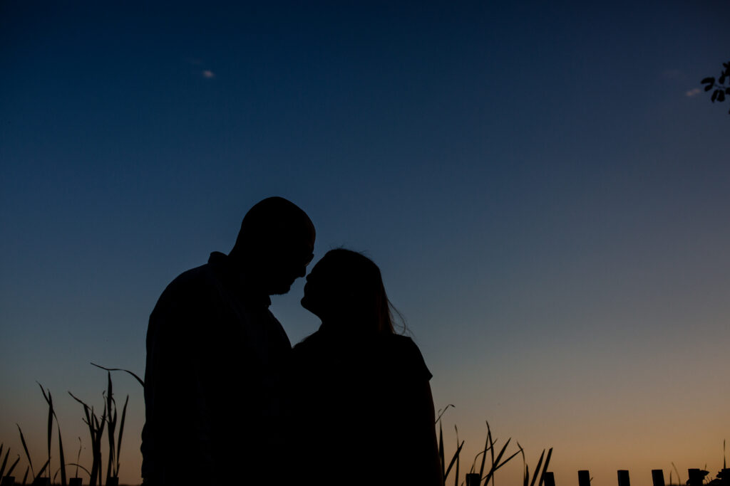 The silhouette of a couple at sunset leaning in to kiss 