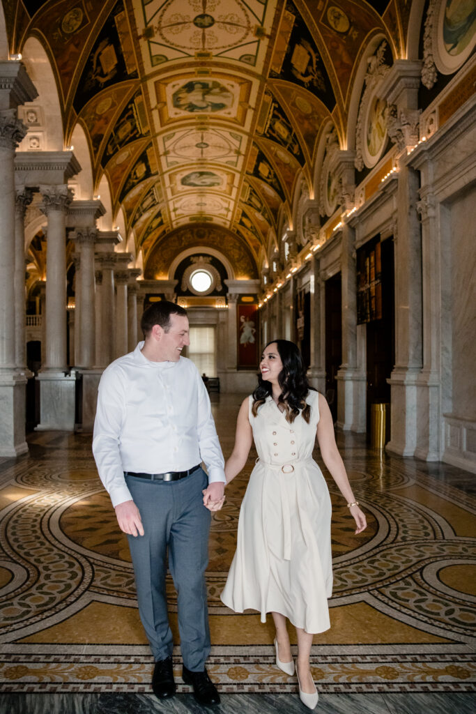 A couple holding hands and walking through the hallway of a grand building 