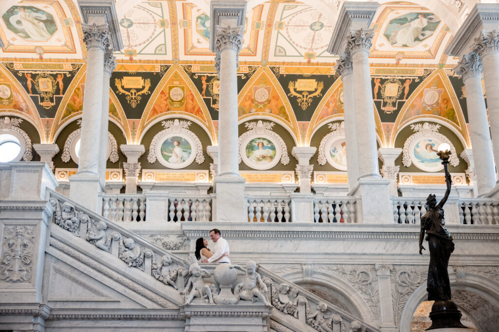 A couple with their arms around each other standing in the middle of a grand staircase in the Library of Congress