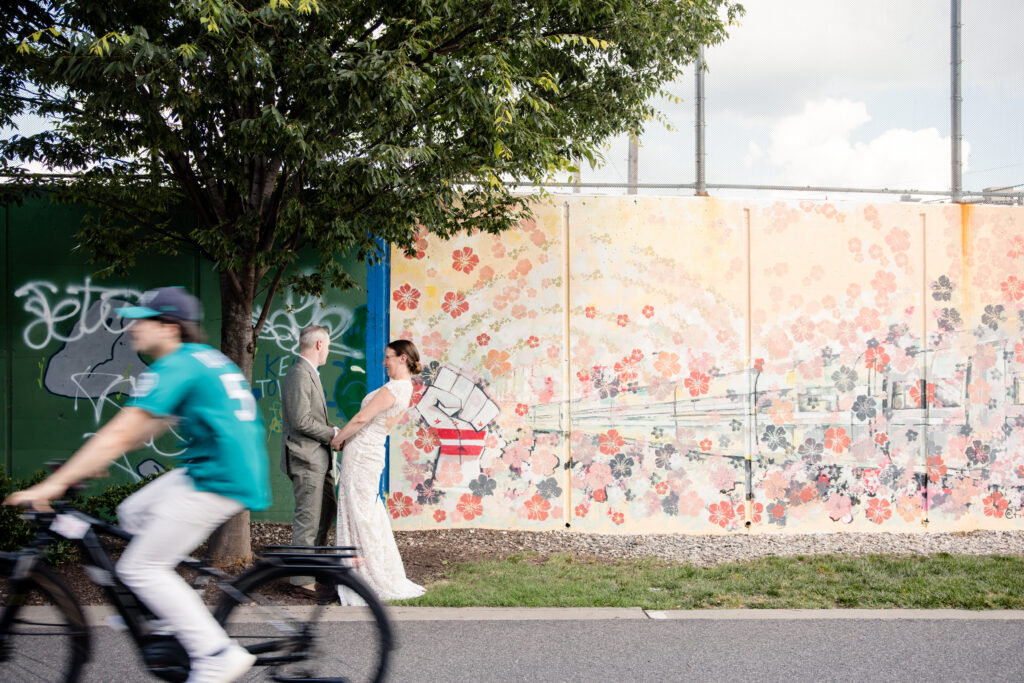 A person biking past a couple holding hands and laughing together on a sidewalk 
