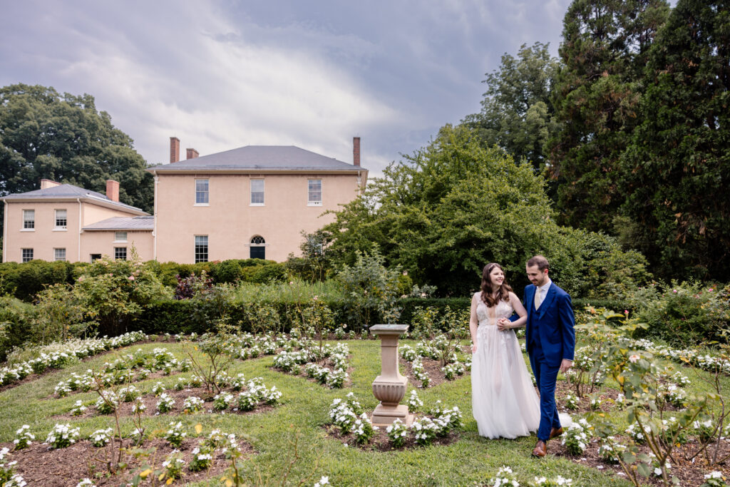 A couple holding hands and walking through a small garden as they laugh 