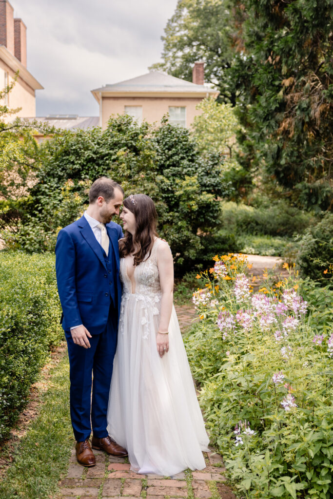 A couple smiling and standing forehead to forehead on a garden path 