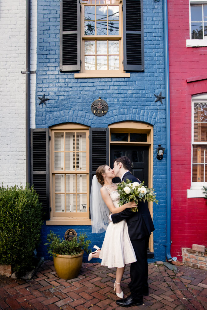 Newlyweds kissing in front of brightly colored townhomes
