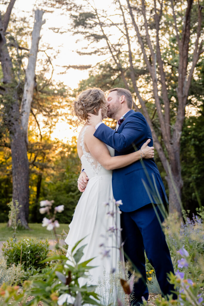 Newlyweds kissing in a wooded area at sunet 
