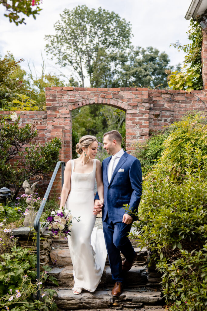 Newlyweds holding hands and walking down a small staircase in a garden 
