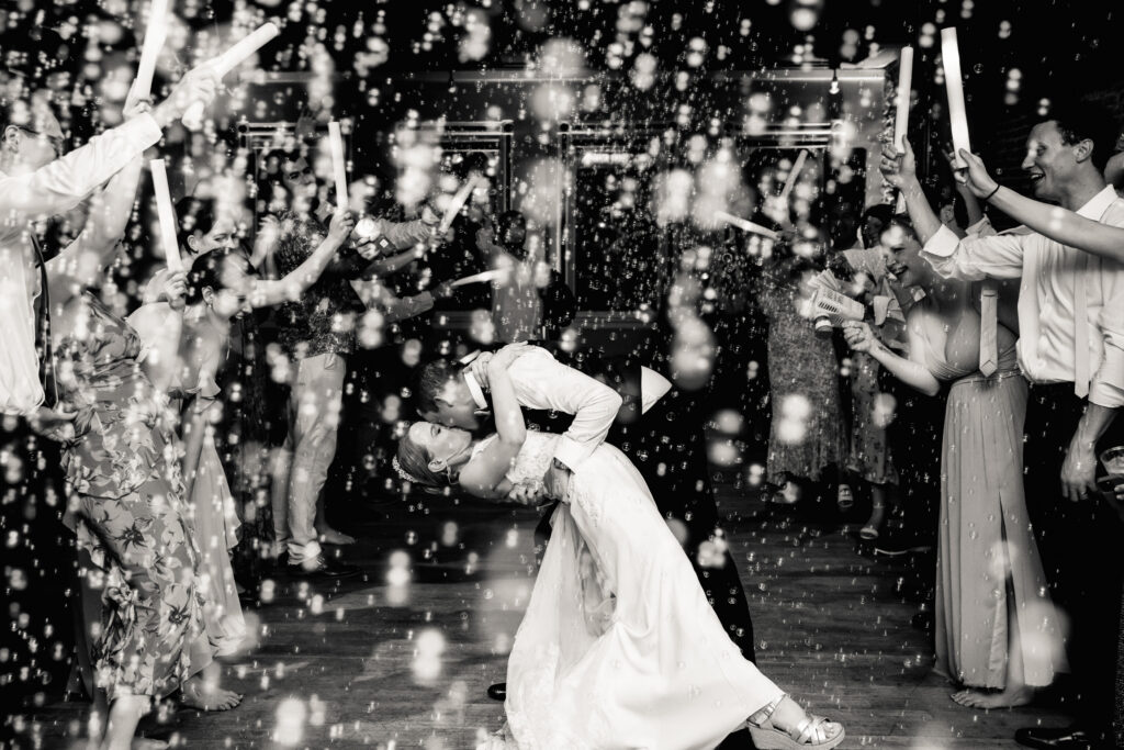 A newlywed dipping their partner and kissing them while their guests cheer around them 
