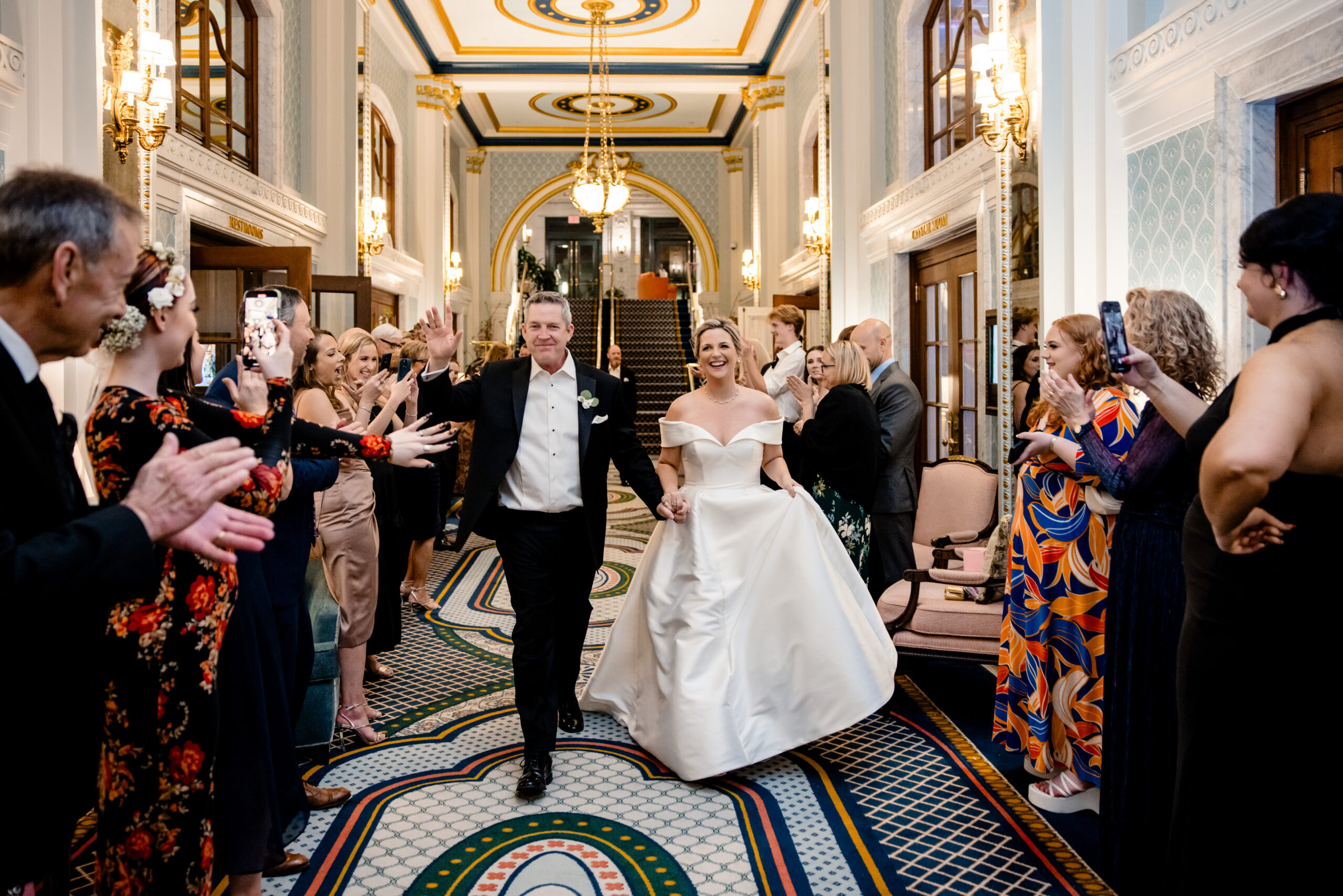 Newlyweds celebrating as they walk down a hallway in between their wedding guests